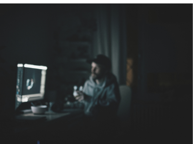 暗い部屋でパソコンを見ている男性の画像